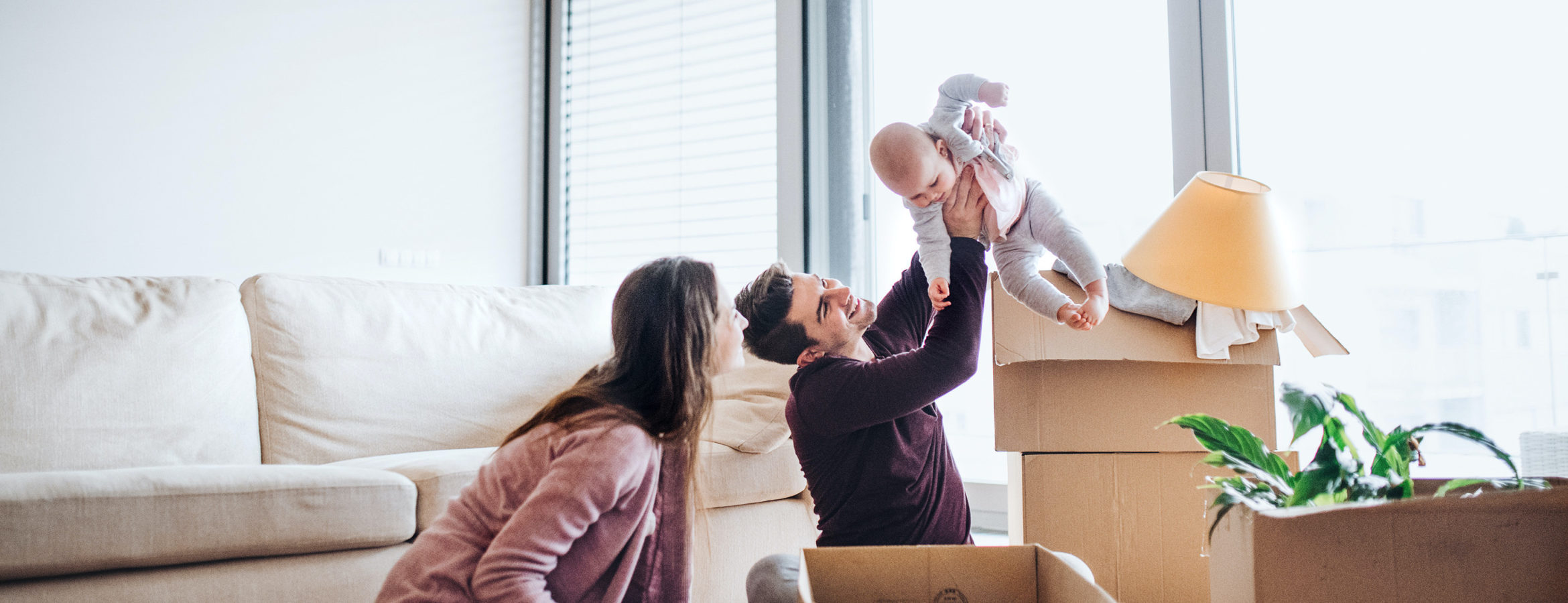 Young couple with a baby and cardboard boxes moving in a new home.