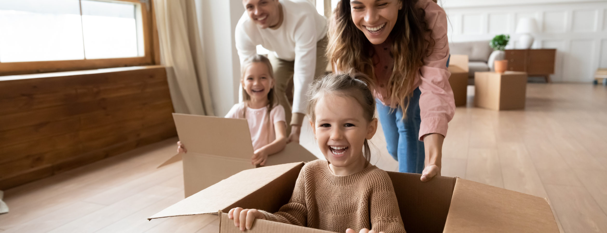 Happy parents playing with little kids riding in box